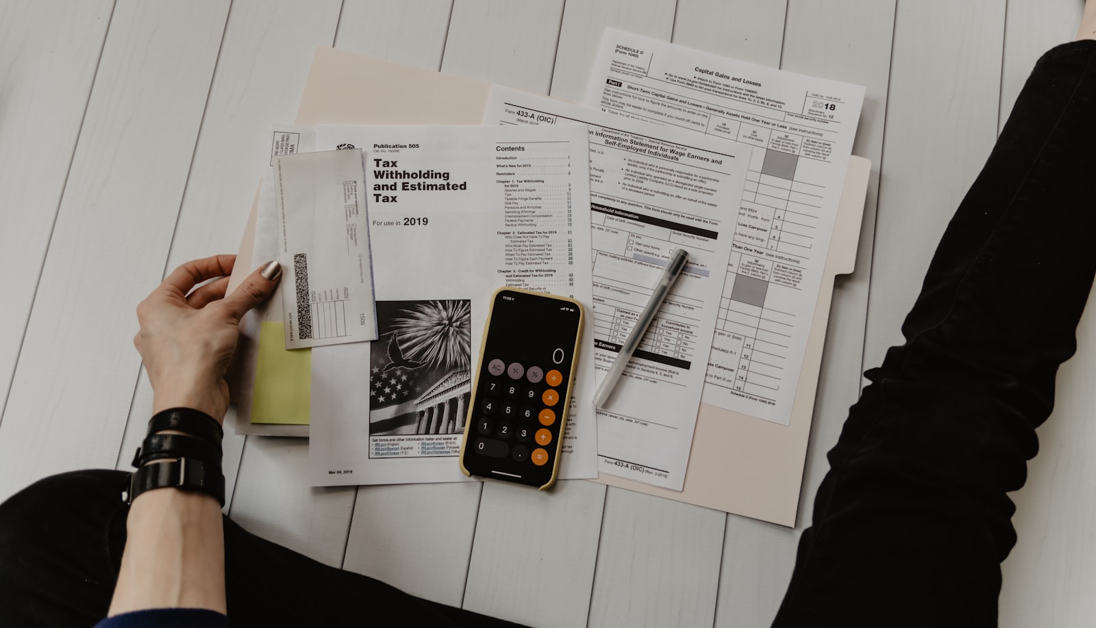 A person planning a marketing budget with a calculator, pen, and printed figures on a desk